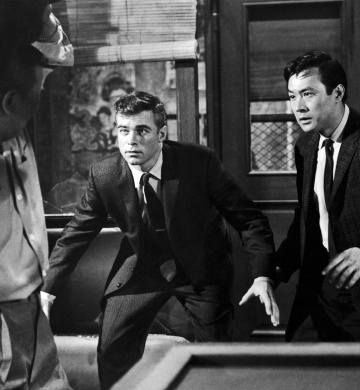 A casually dressed man is throwing something heavy at two men dressed in suits